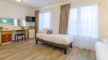 Une chambre d’hôtel équipée d’un lit, d’un bureau, d’une chaise, d’une télévision et de grandes fenêtres avec des rideaux.