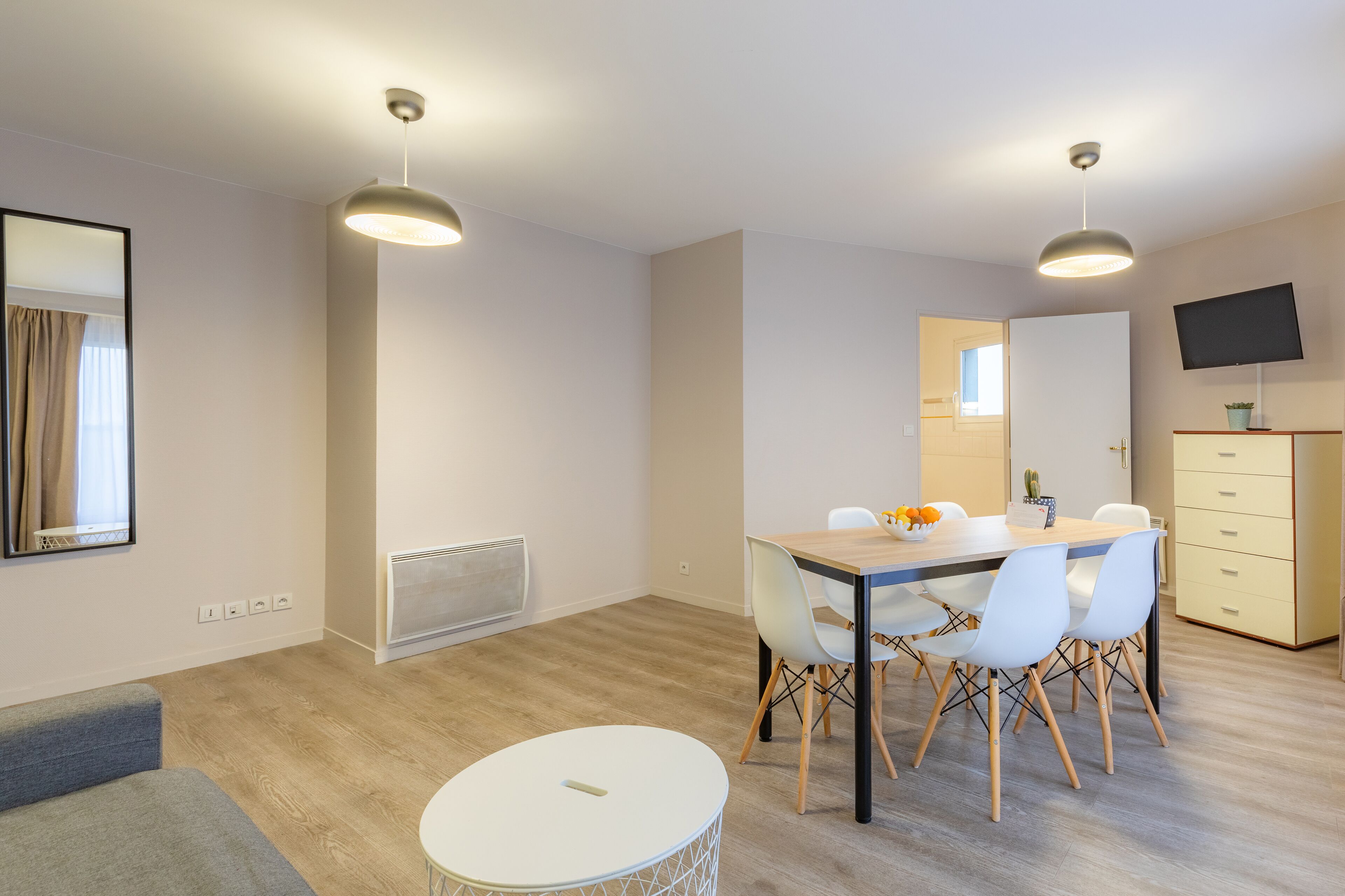Habitació moderna i ben il·luminada amb taula de dinar, cadires, una taula rodona petita, sofà, televisió i armari.