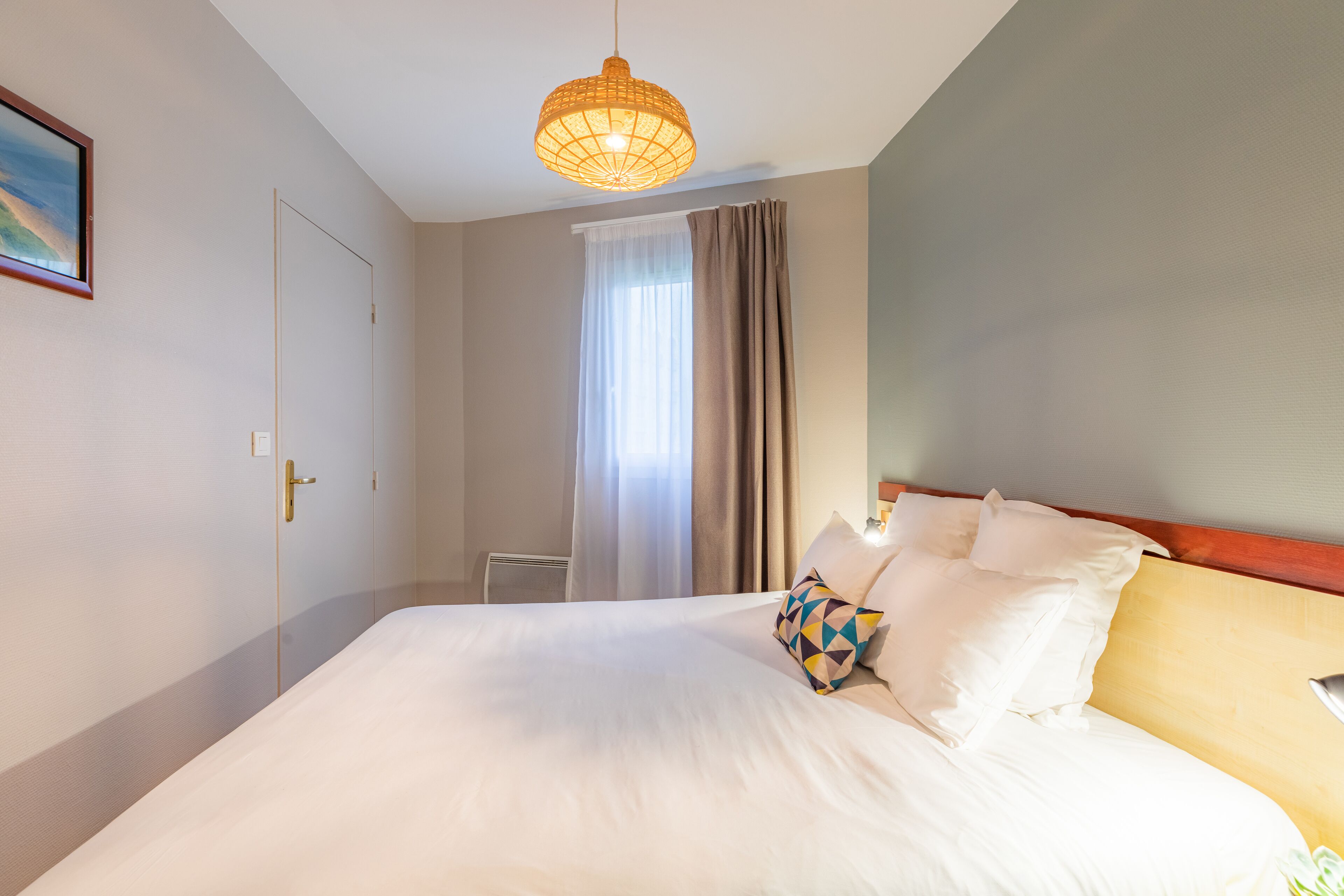 Une chambre d’hôtel avec un grand lit, une table de chevet, une lampe, une fenêtre avec des rideaux et un tableau au mur.