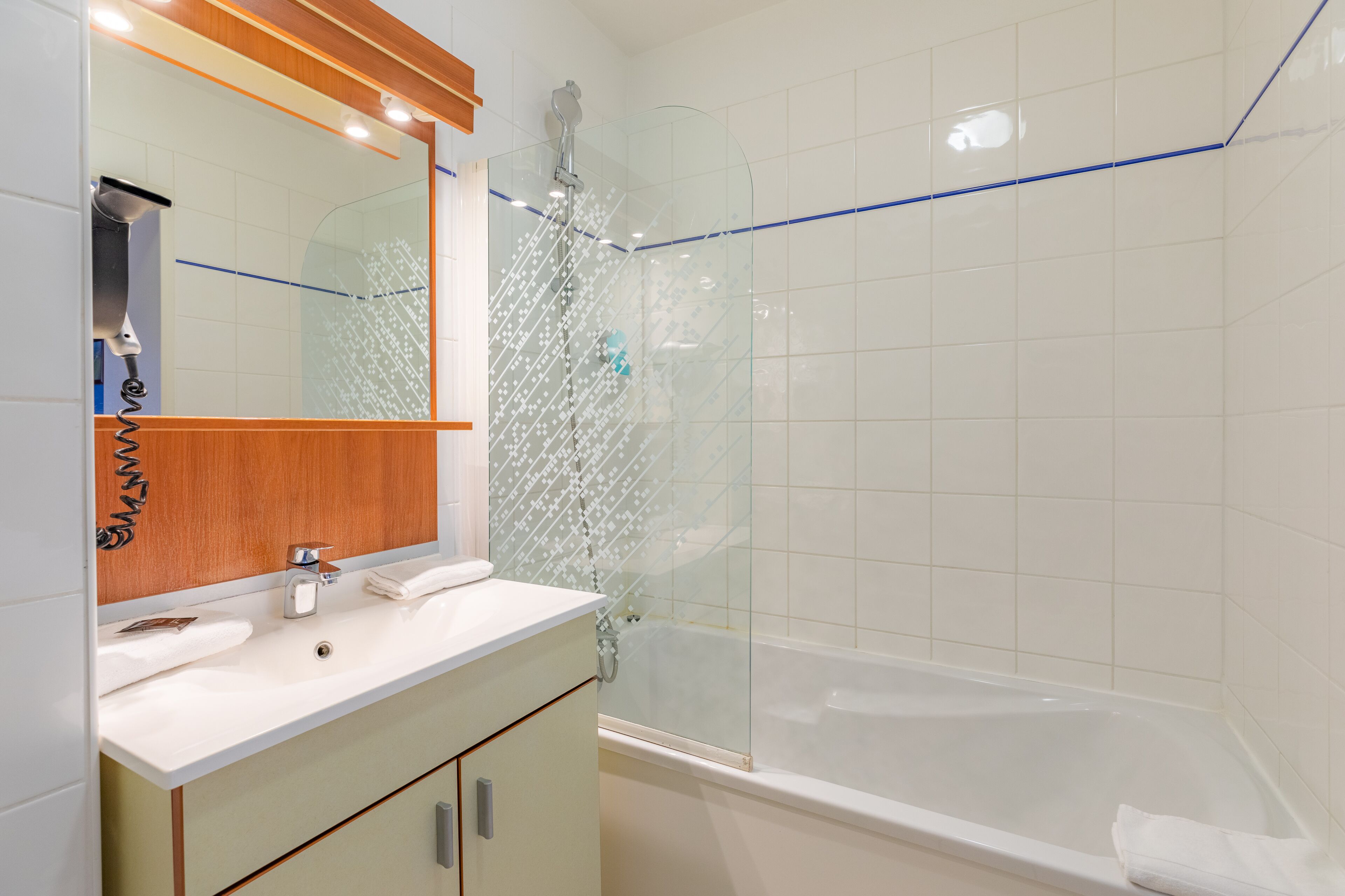 Un bagno con doccia vetro, lavandino bianco e mobile contenitore in legno.