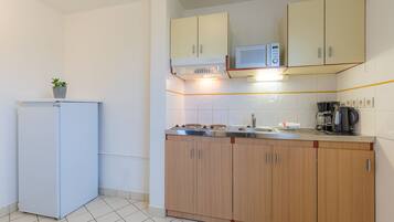 A compact kitchen with a refrigerator, microwave, stove, and wooden cabinets.