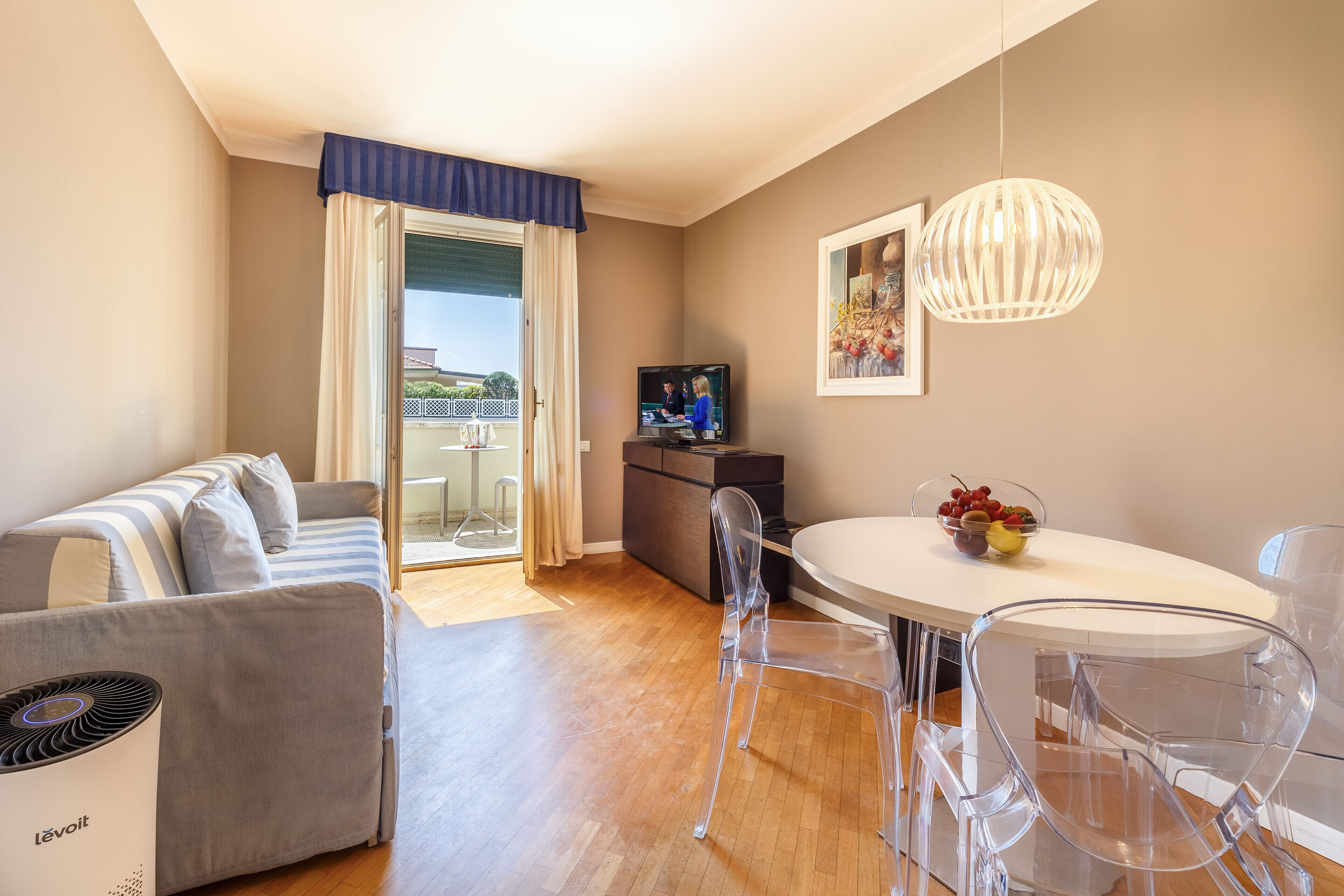 Una sala de estar moderna con un sofá, una mesa de comedor con sillas, un televisor y un balcón con vistas.