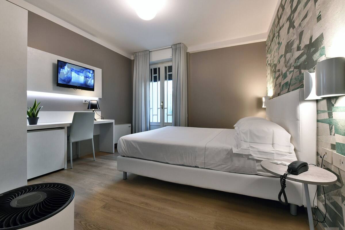 A modern hotel room with a bed, desk, chair, and a television mounted on the wall.