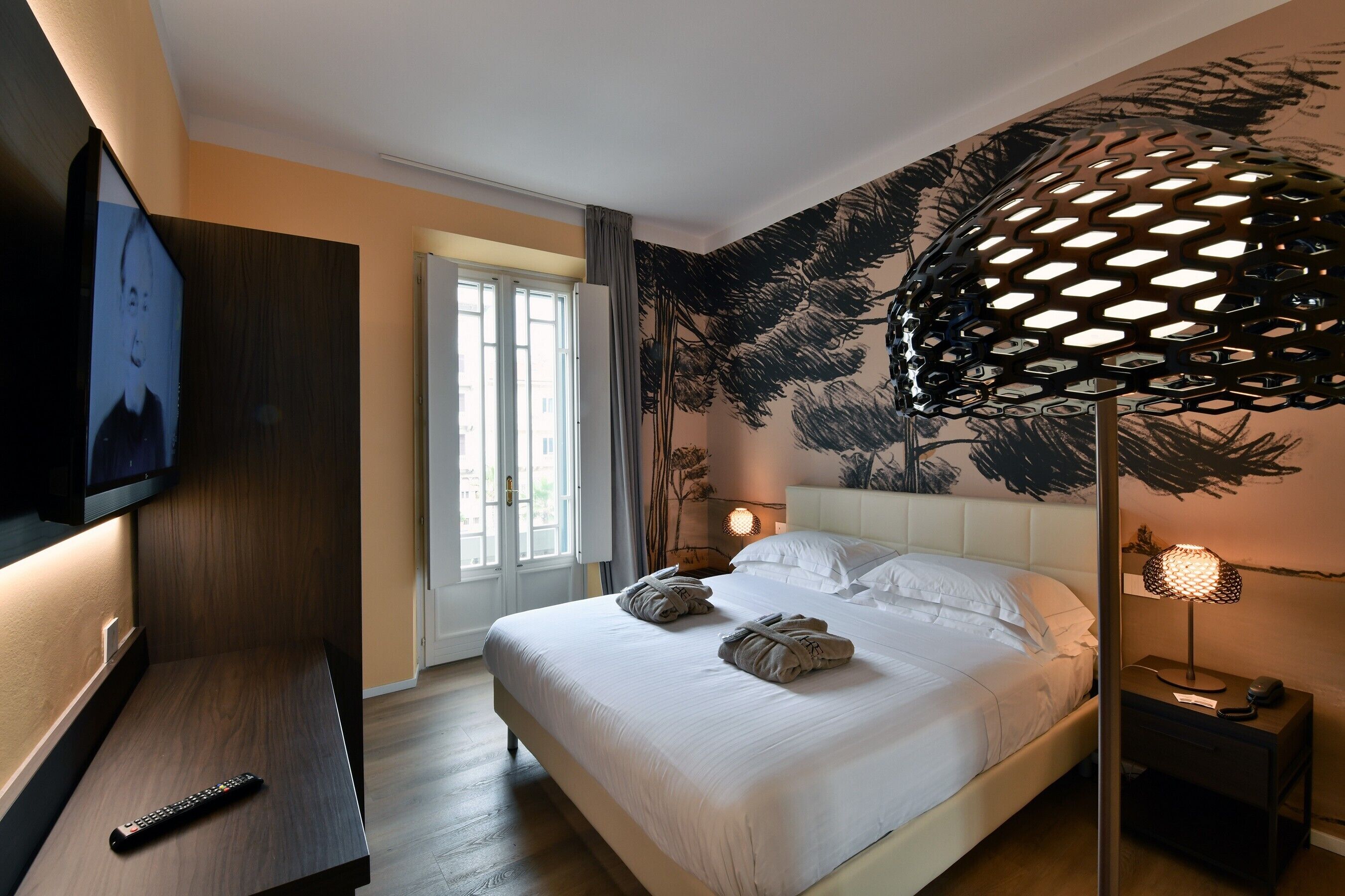 A hotel room with a bed, a TV, a desk, a lamp, and a window.