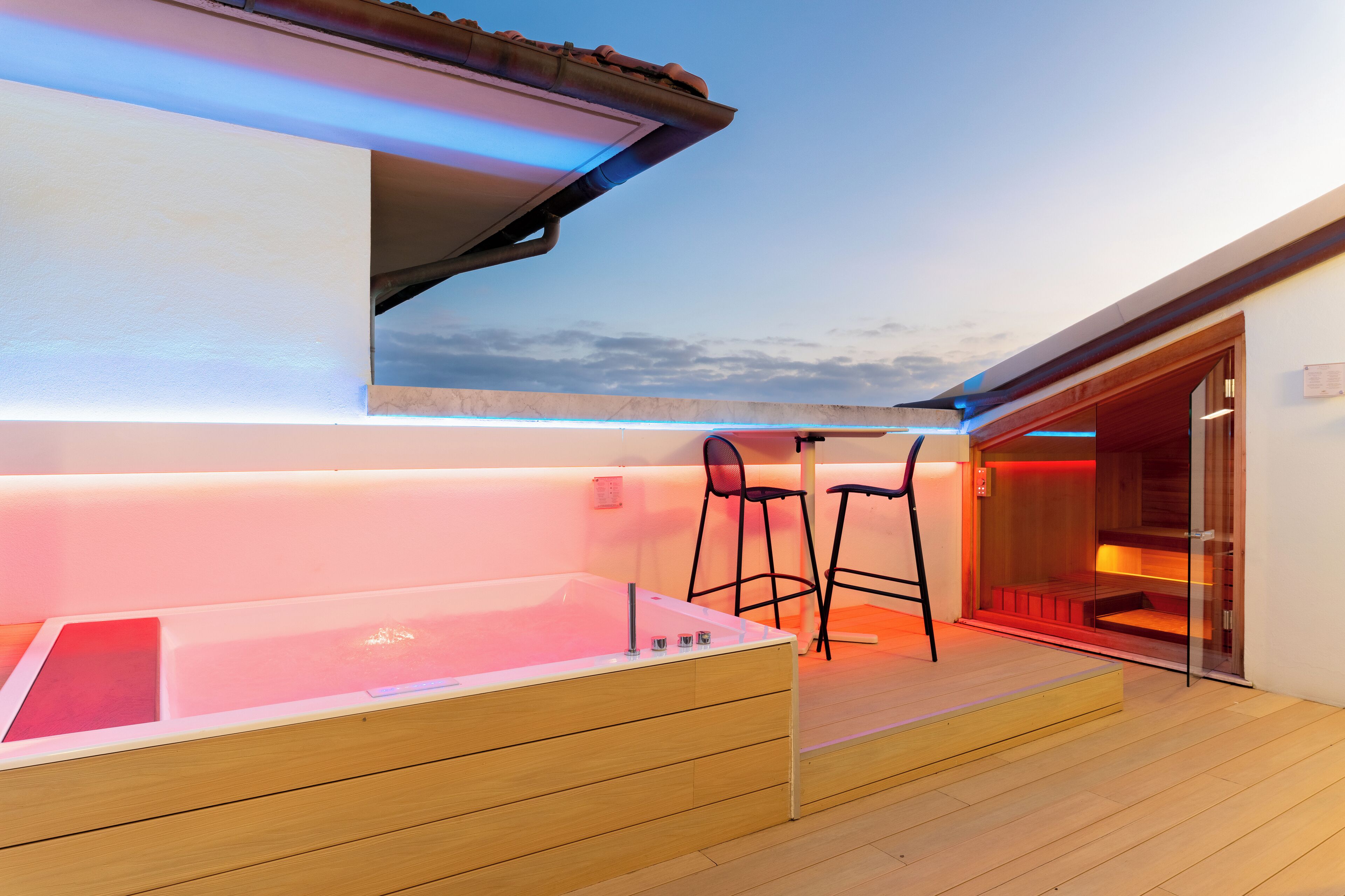 A modern spa area with a hot tub, wooden flooring, and two black bar stools.