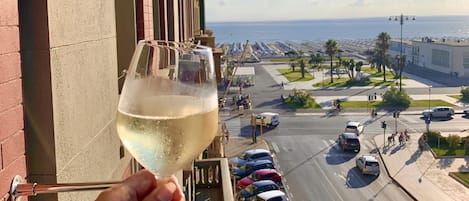 A hand holding a wine glass with a view of a coastal street and parked cars.