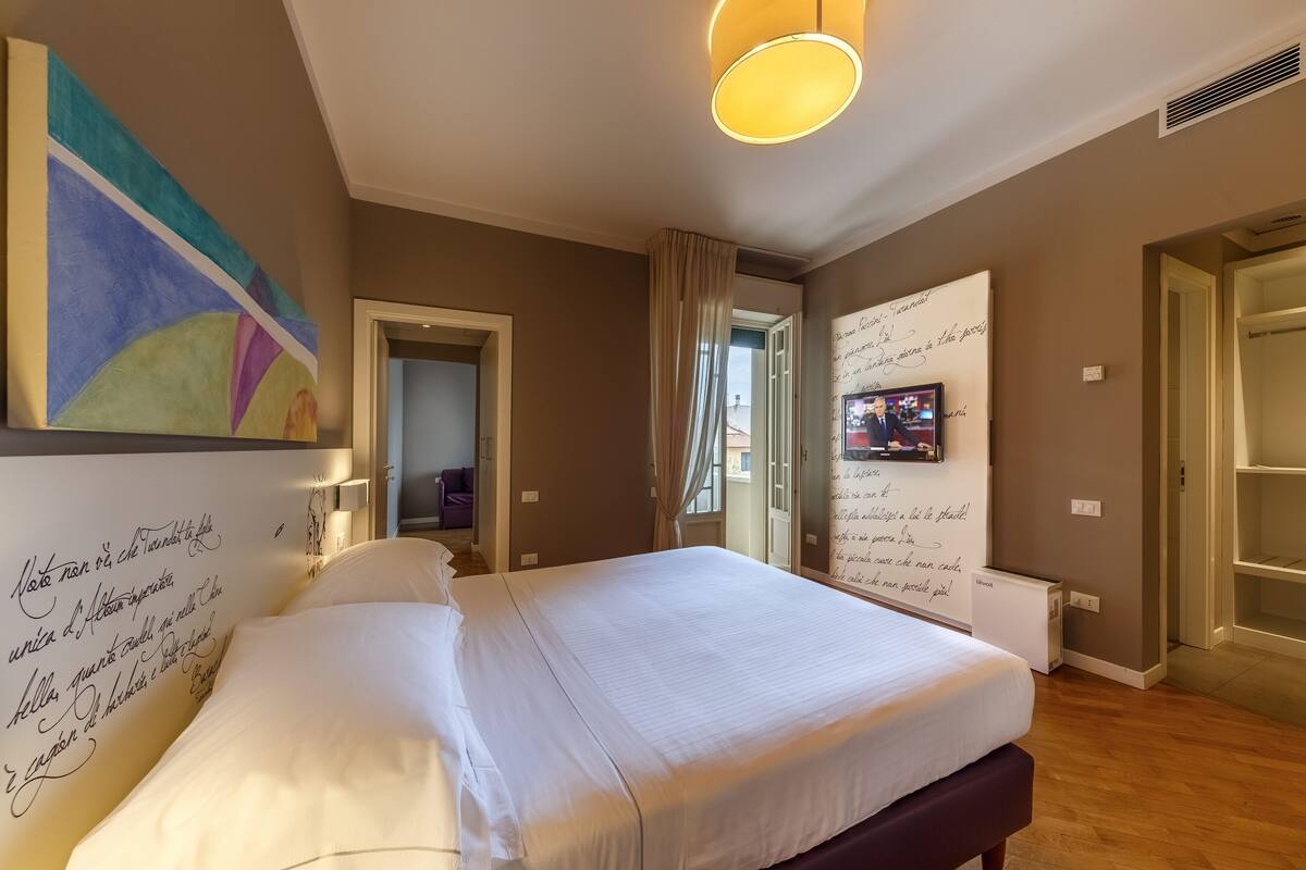 A bedroom with a large bed, a wall with a colorful abstract painting, and a white radiator.