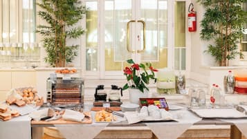 Montaje de un bufé de desayuno con diversos alimentos, una máquina de café y plantas decorativas.