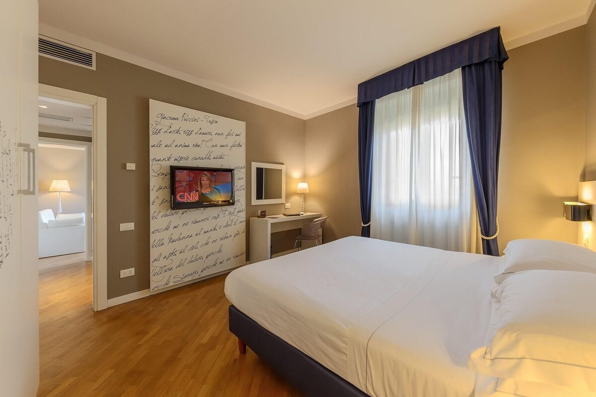 A hotel room with a bed, a desk, a TV, and a wall with handwritten notes.