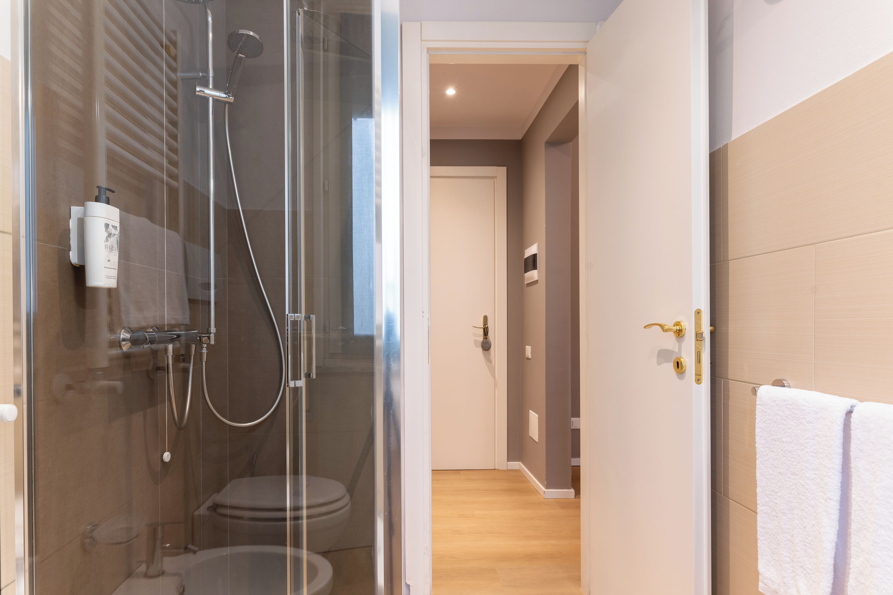 A modern bathroom with a glass-enclosed shower, a toilet, and a towel rack.