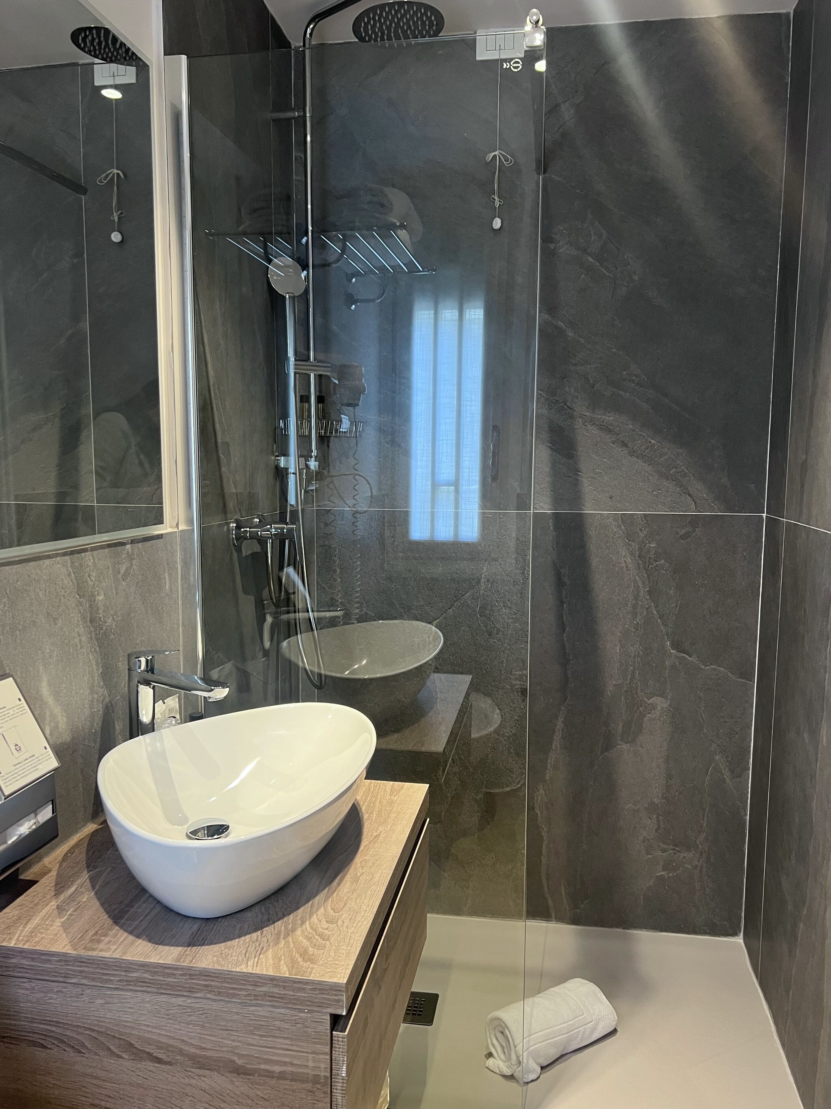 A modern bathroom with a large mirror, a white vessel sink, a glass-enclosed shower, and a towel on the floor.