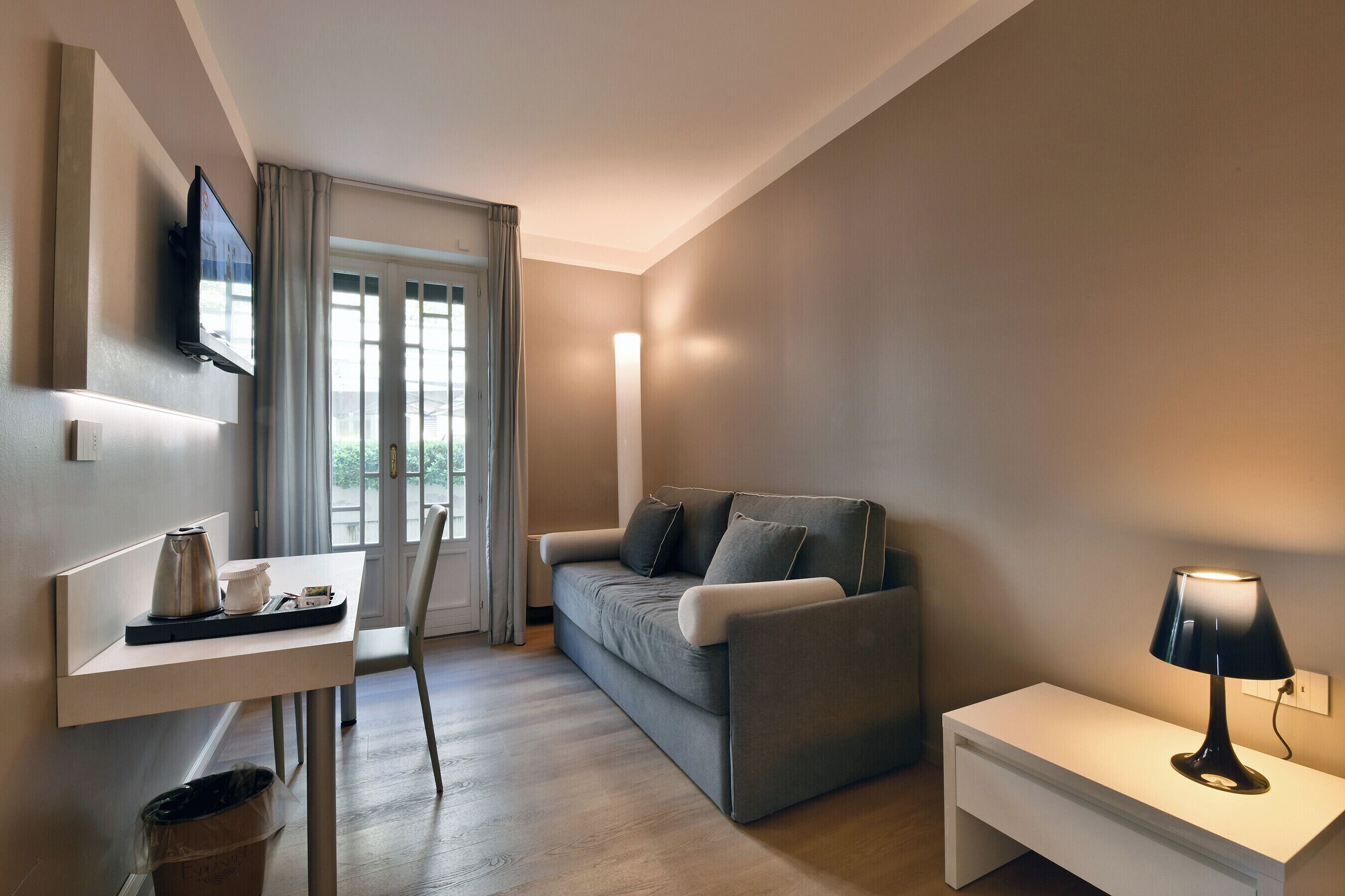 Un salon moderne avec un canapé, une table basse, un téléviseur fixé au mur et une lampe sur une table de chevet.