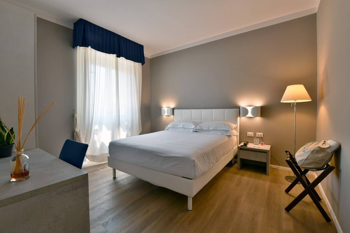 A modern bedroom with a bed, bedside lamps, a bedside table, and a chair.