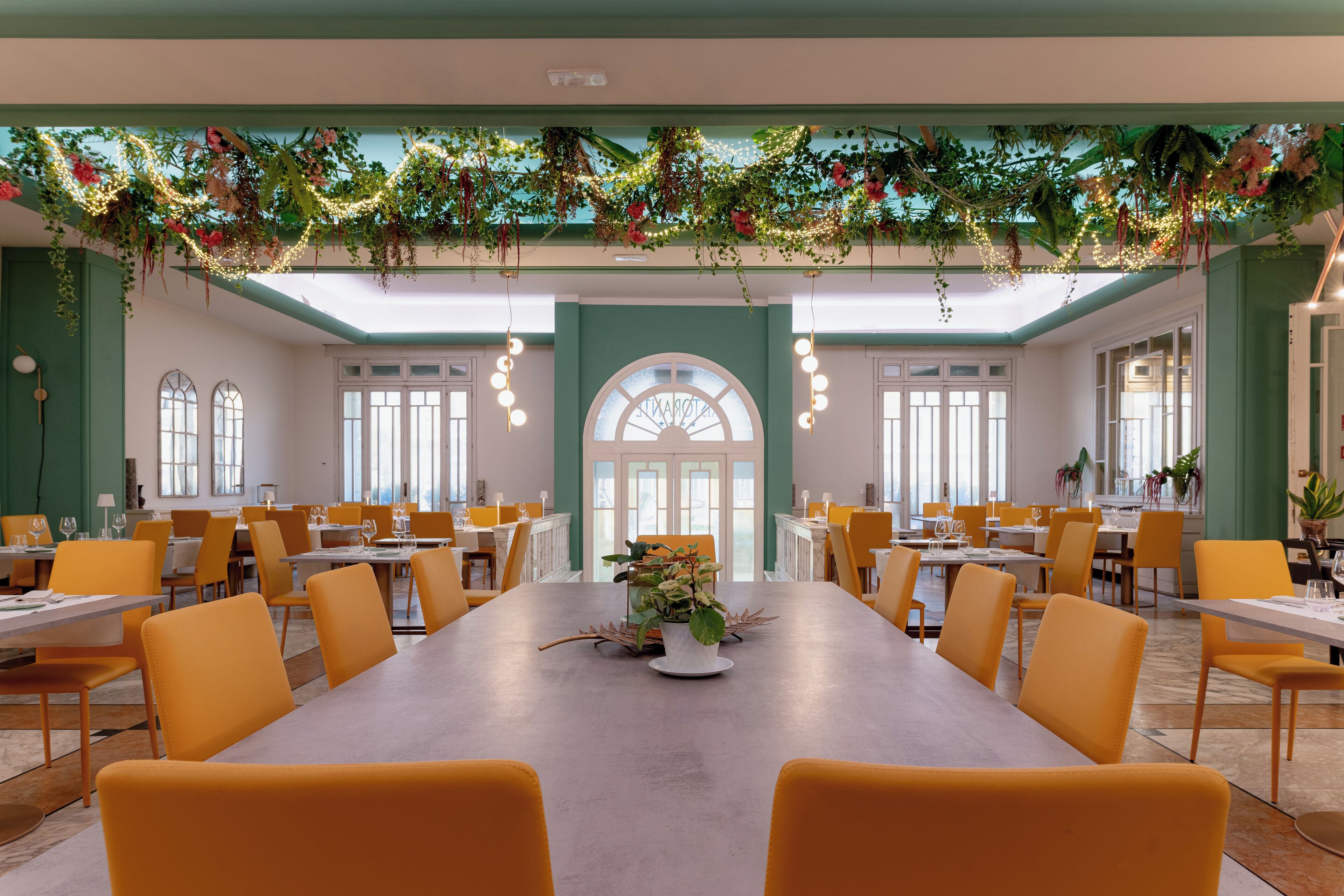Un vaste espace dédié à la salle à manger, avec une longue table, des chaises jaunes et une plante décorative en guise de centre de table.