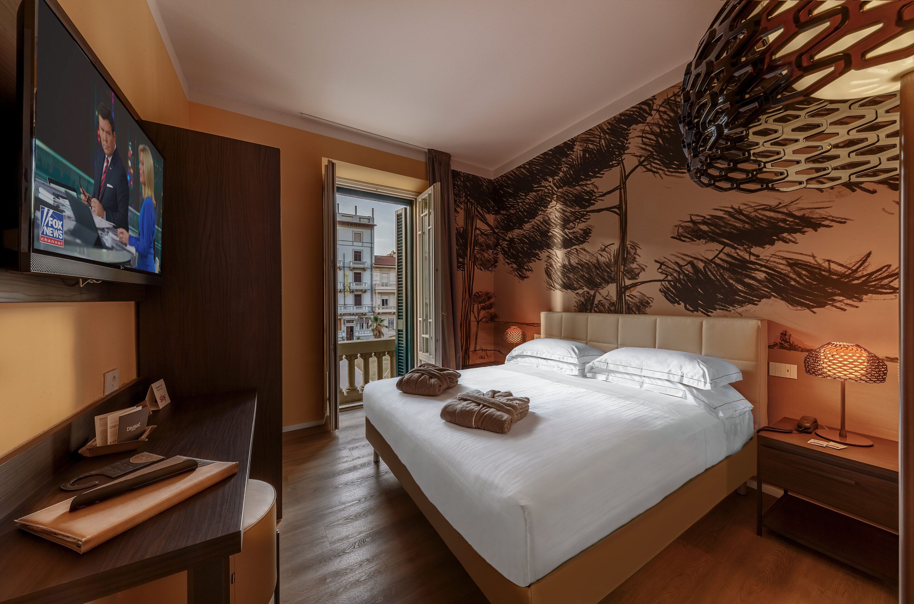 A hotel room with a bed, a desk, a TV, and a view of the outside.