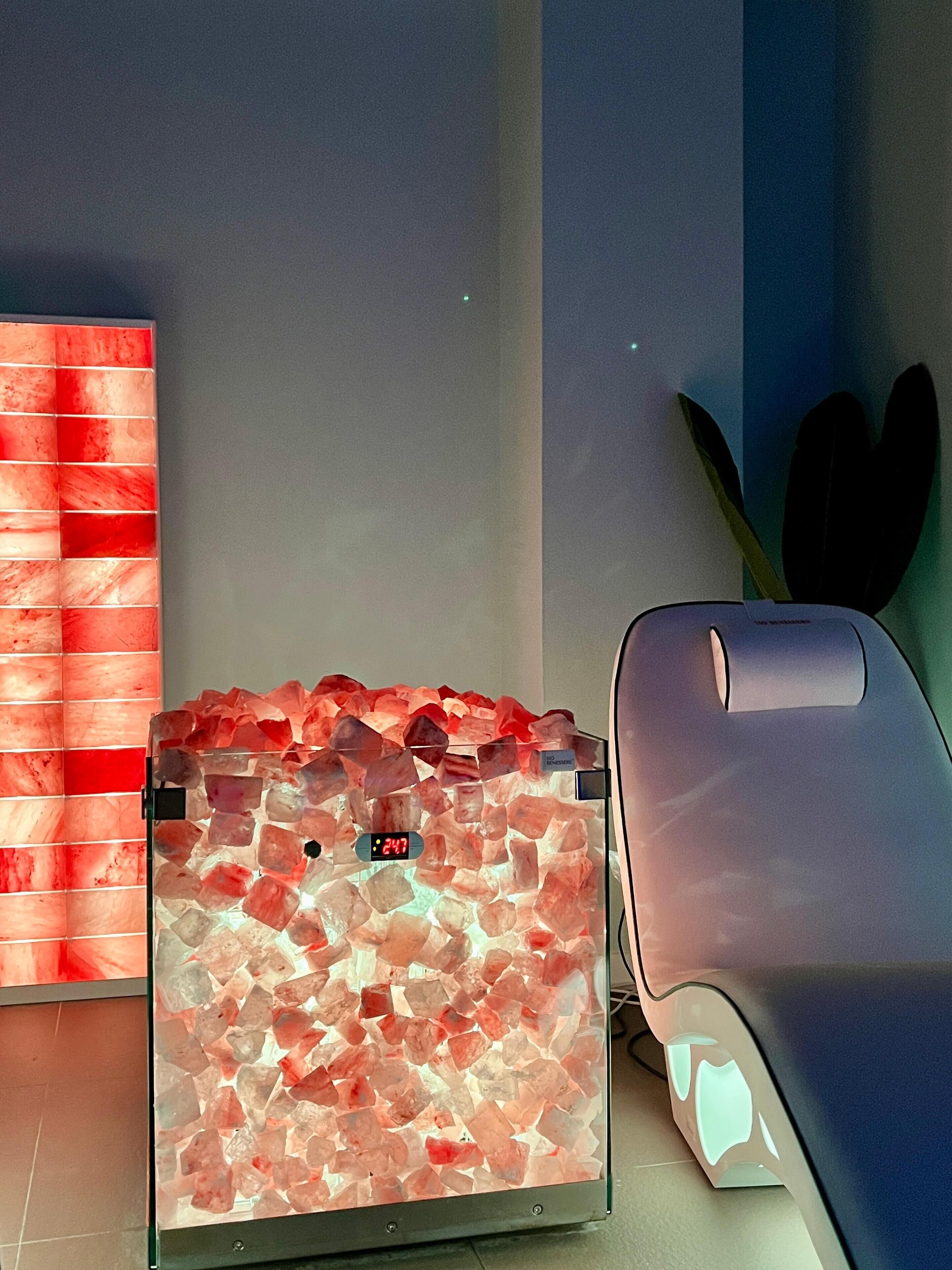 Una silla de masaje con pantalla digital, un recipiente de vidrio con cristales rojos y una pared con diseño rojo y blanco.