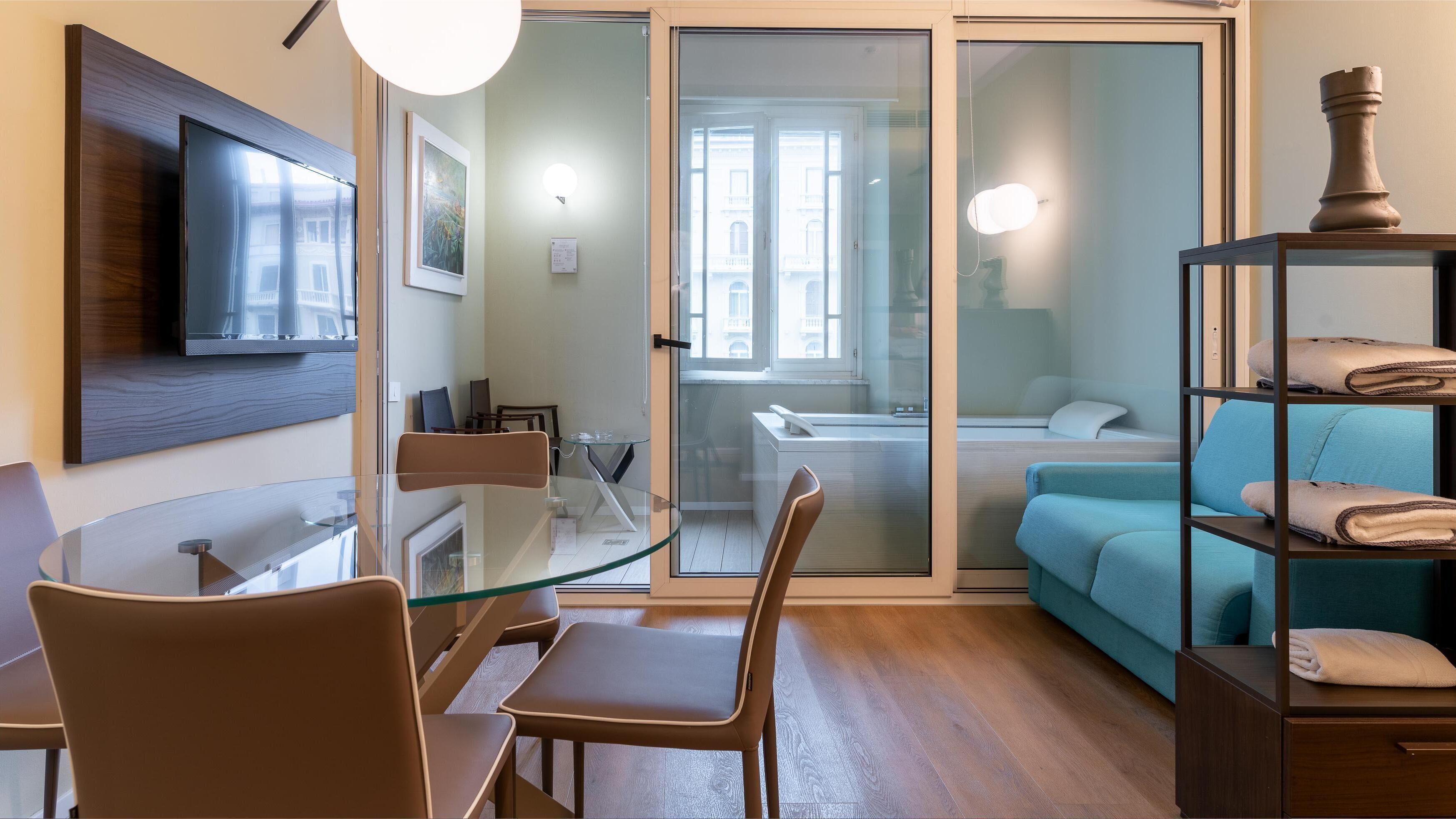 Una sala de estar moderna con una mesa de comedor de vidrio, un sofá y un televisor montado en la pared.