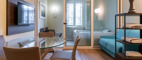 Una sala de estar moderna con una mesa de comedor de vidrio, un sofá y un televisor montado en la pared.