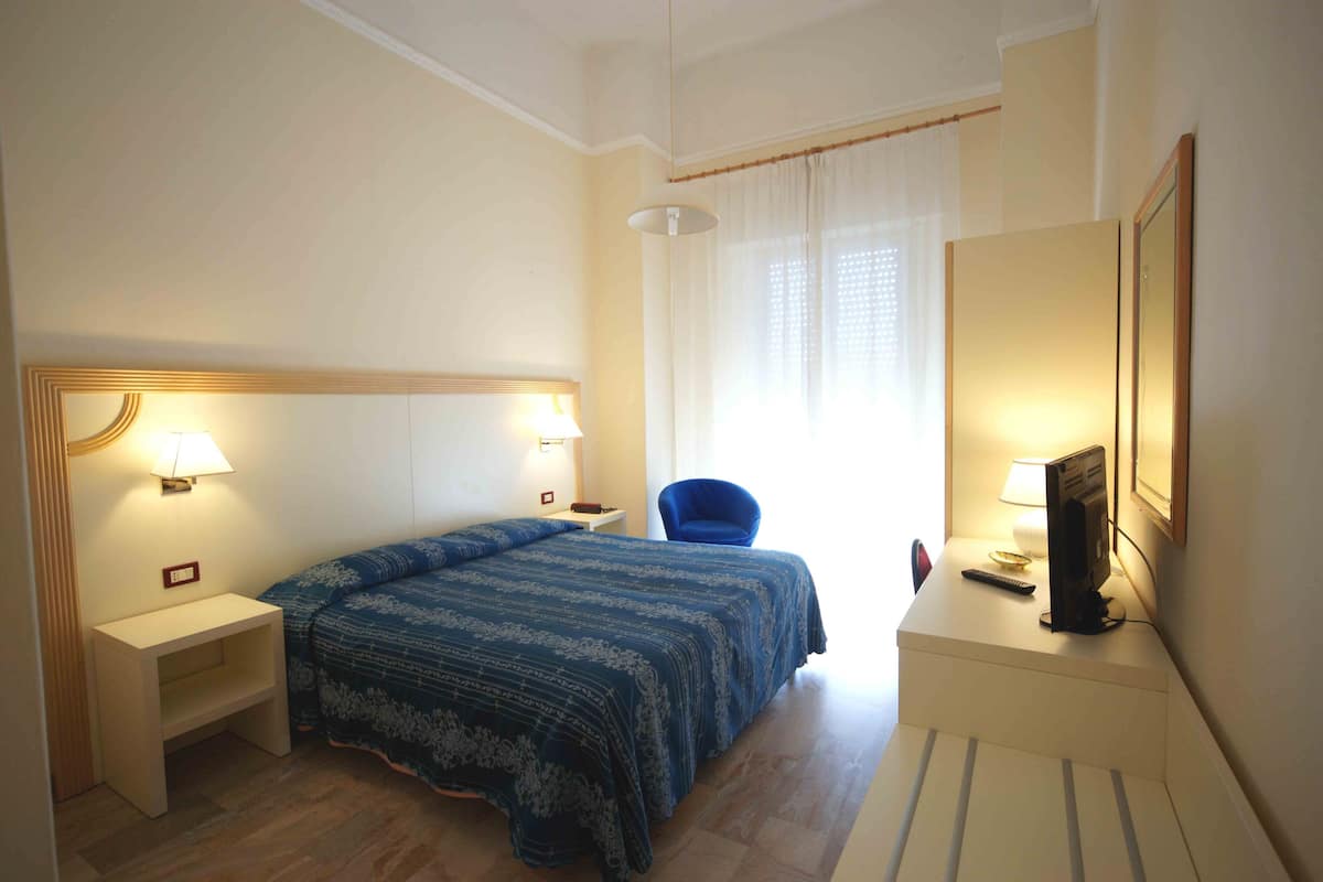 Une chambre d’hôtel avec un lit, un bureau, une chaise, une télévision et une fenêtre avec des rideaux.