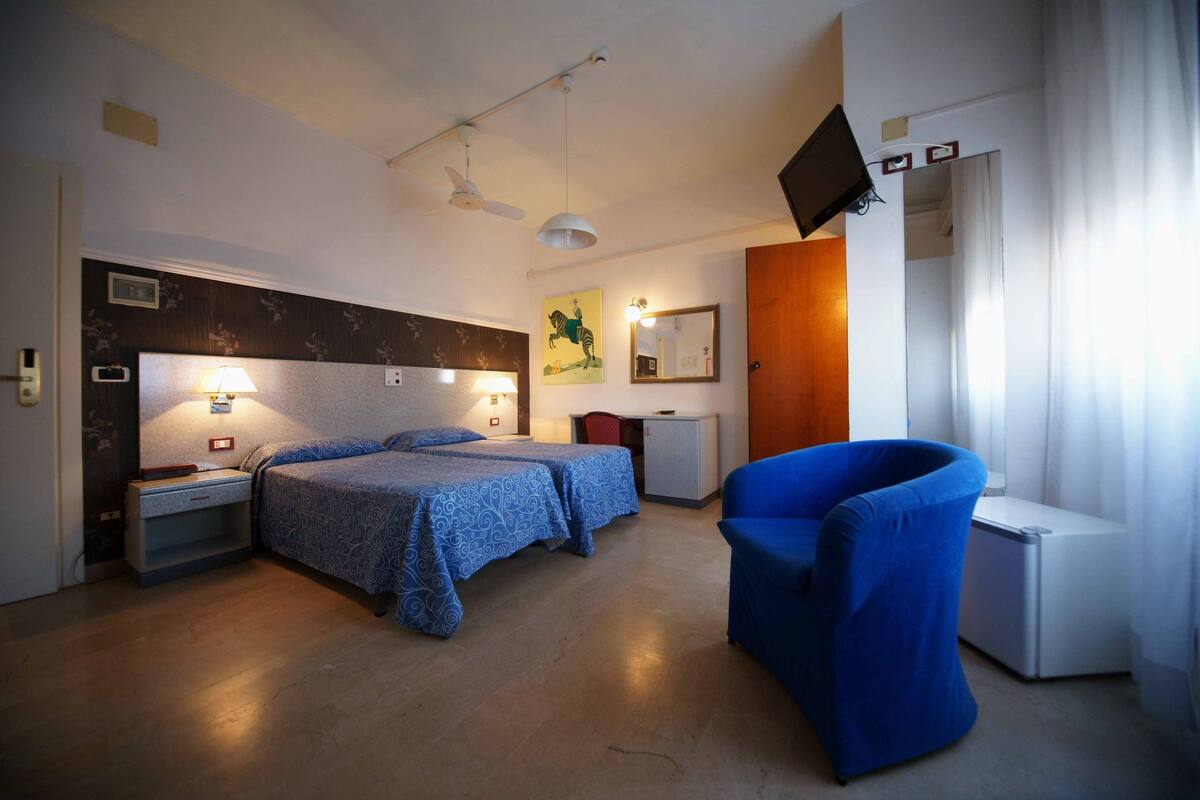 Une chambre d’hôtel avec deux lits, un bureau, une chaise, une télévision et un ventilateur de plafond.
