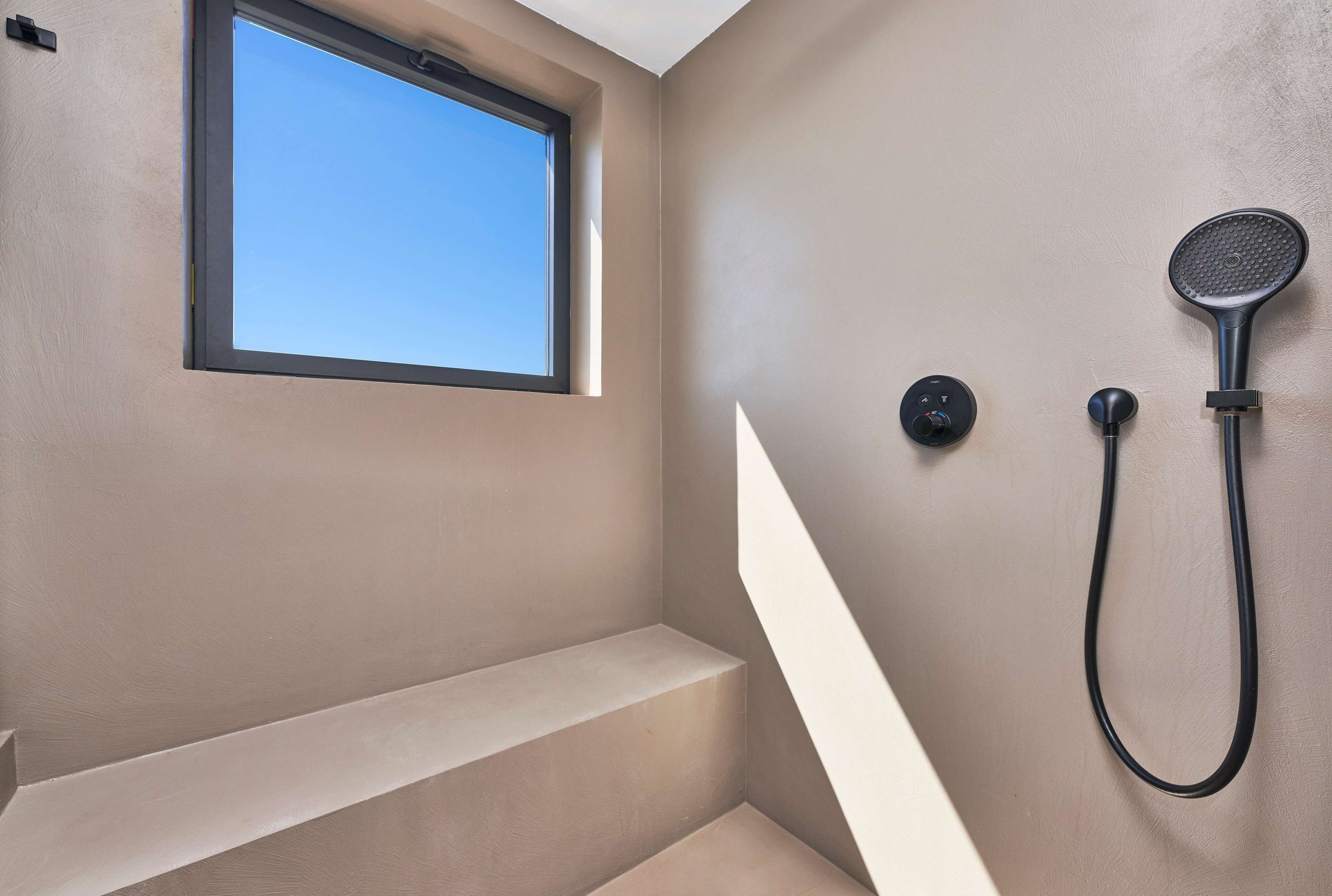 Un baño con ventana integrada, ducha con cabezal de ducha de mano y panel de control.