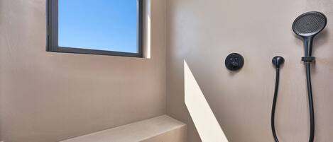 Un baño con ventana integrada, ducha con cabezal de ducha de mano y panel de control.