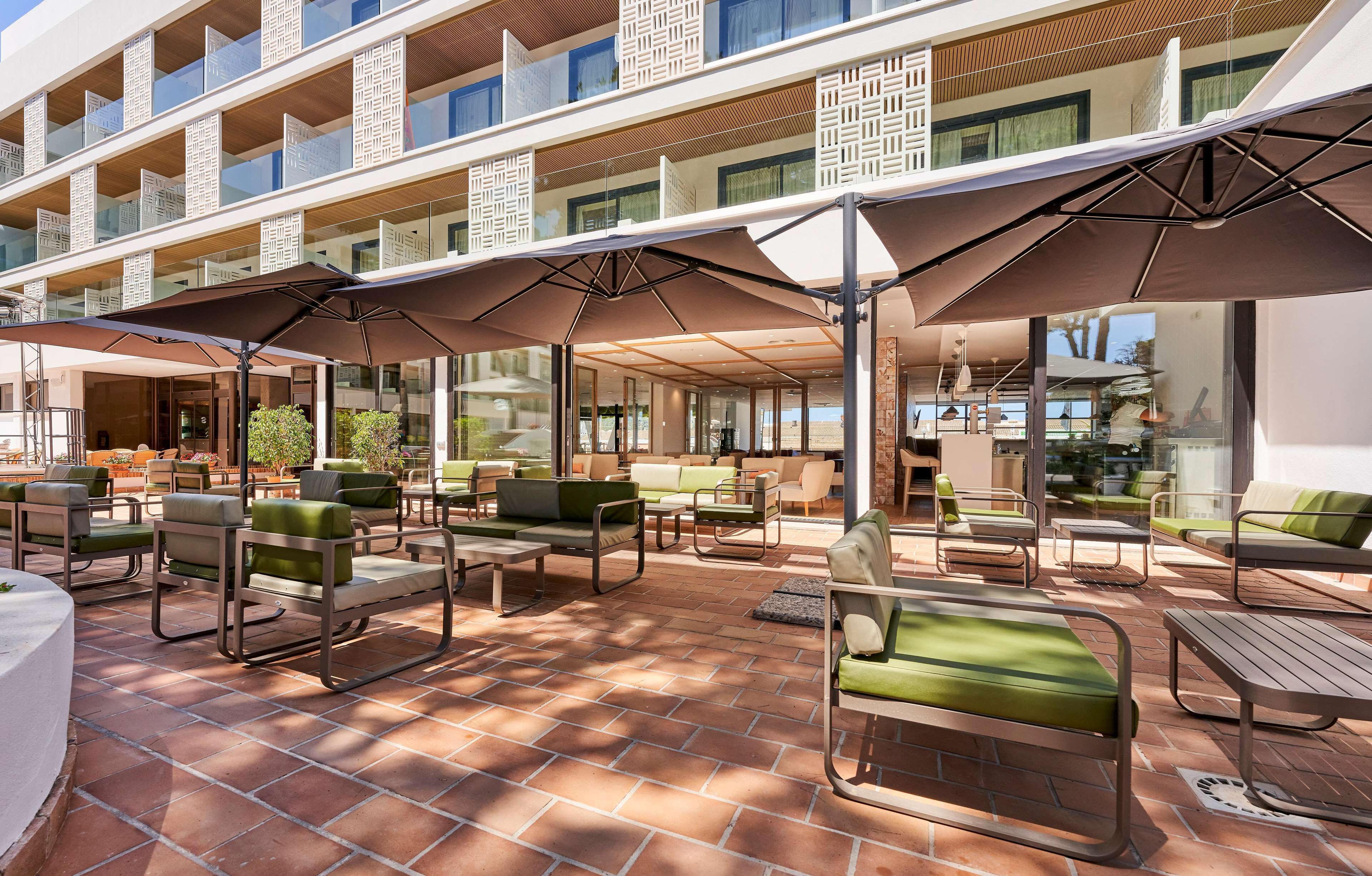 Un patio de hotel con mobiliario exterior, incluyendo sillas y mesas, y una zona de piscina.