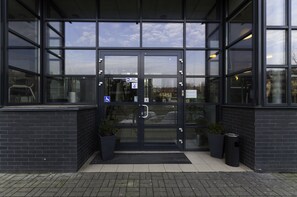 Une entrée moderne avec des portes vitrées, une rampe d’accès pour les personnes à mobilité réduite et des plantes en pot.