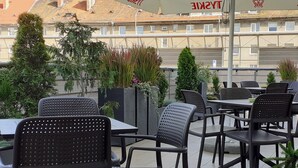 An outdoor seating area with black chairs and tables, surrounded by potted plants and a building in the background. - Weiser Hotel (Wroclaw)