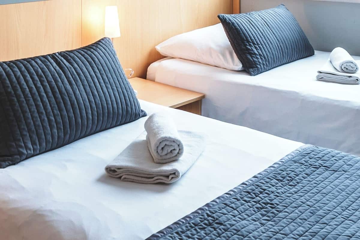 A hotel room with two beds, each with a pillow and a rolled towel.