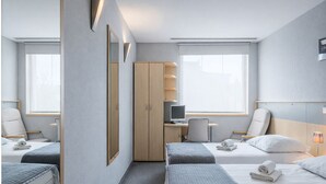 A hotel room with two beds, a desk with a computer, a wardrobe, and a window with a view. - Weiser Hotel (Wroclaw)