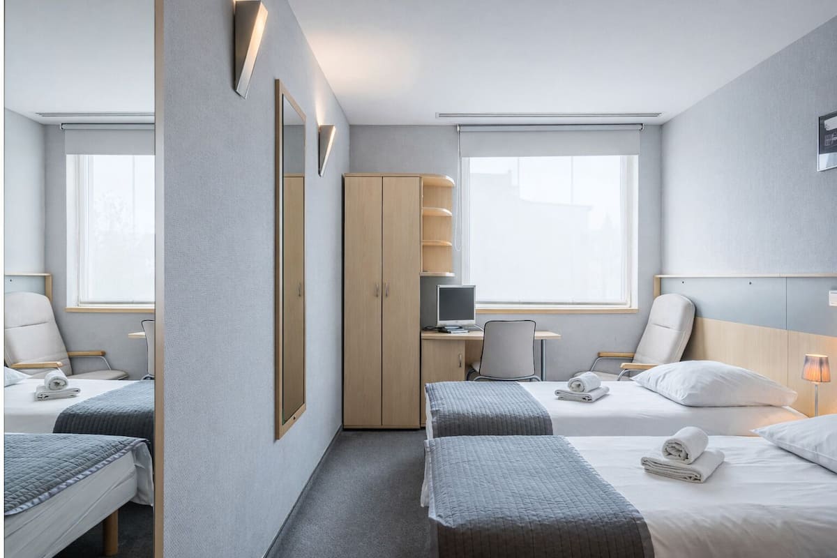 A hotel room with two beds, a desk with a computer, a wardrobe, and a window with a view.