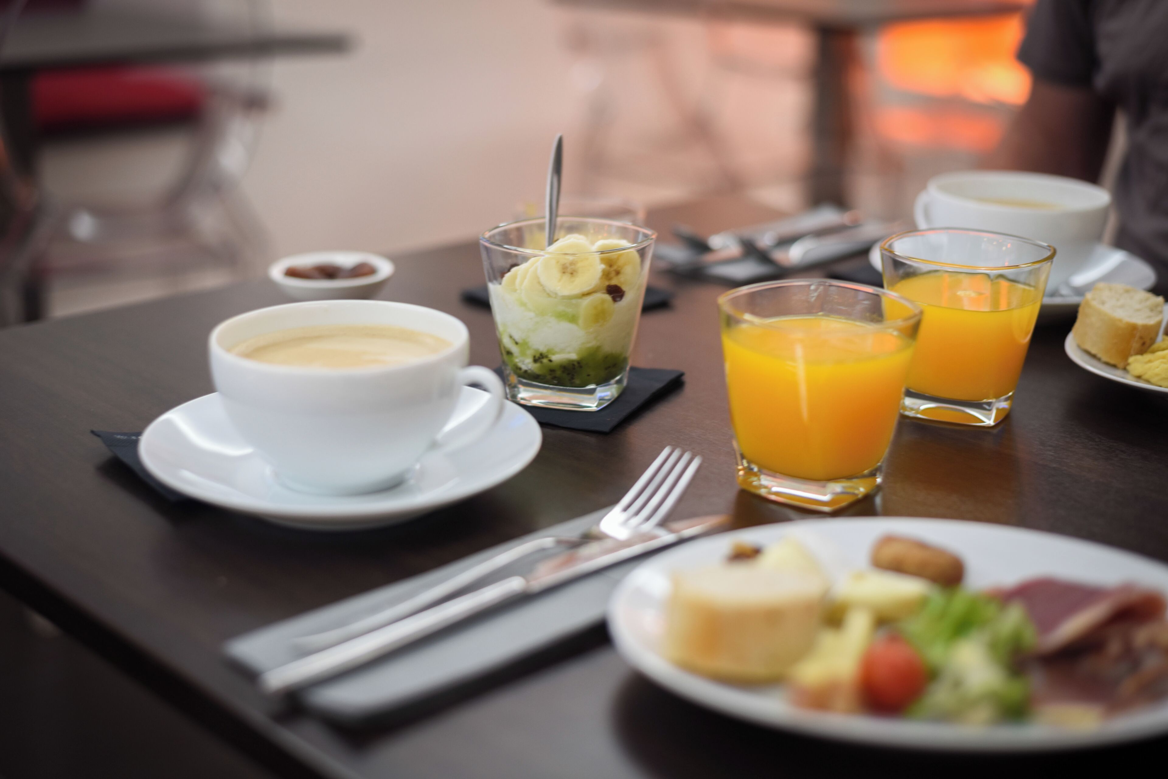 Une table mise pour le petit-déjeuner avec une tasse de café, un verre de jus d’orange, une assiette de nourriture et une fourchette.
