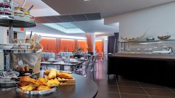 Un bufé de desayuno moderno con diversas opciones de comida y un área de estar con sillas transparentes.