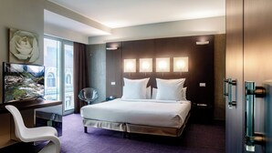 A hotel room with a large bed, a desk with a chair, a TV, and a view of a mountain through the window. - Le Rex Hotel (Tarbes)