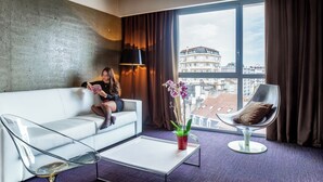 A modern hotel room with a white sofa, a glass coffee table, a modern chair, and a large window with curtains. - Le Rex Hotel (Tarbes)