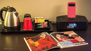 A table with a kettle, red cup, Nescafé coffee pods, a Philips digital clock, and a magazine.