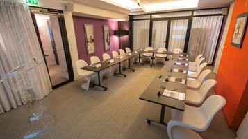 A conference room with a long table, white chairs, and a projector screen.