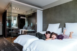 Habitación de hotel moderna con una cama grande, zona de ducha con cerramiento de vidrio y una pared oscura con textura.