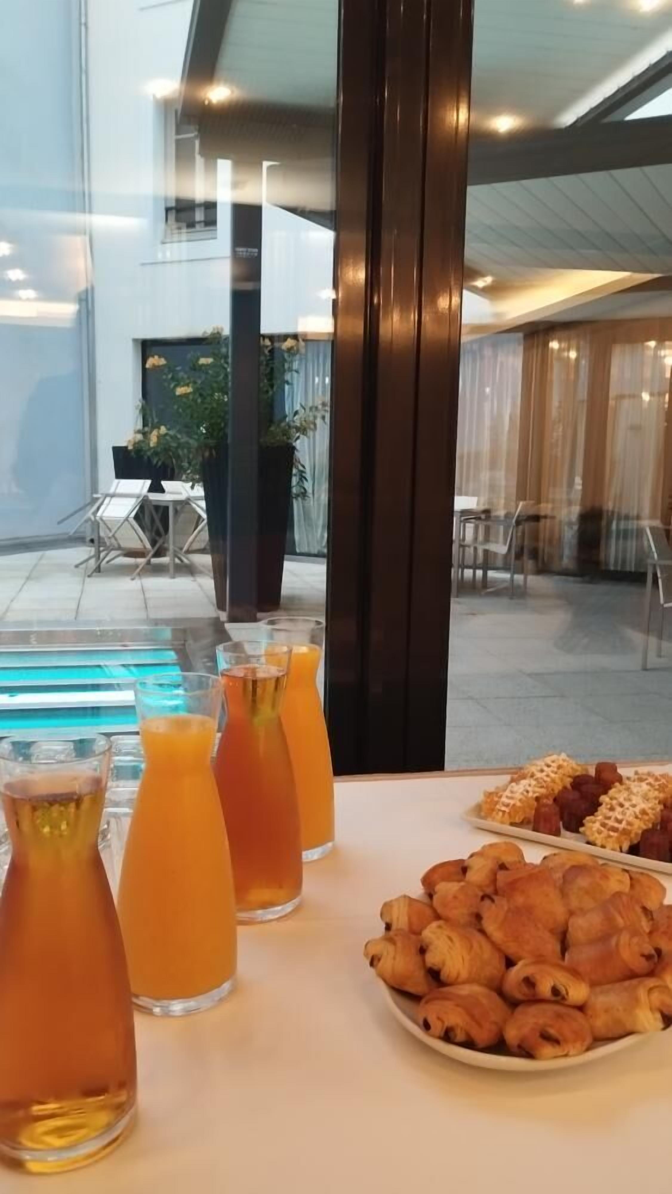 A table with drinks and pastries, a pool, and outdoor seating.