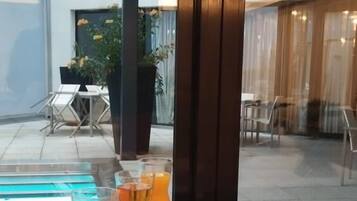 Et bord med drikkevarer og bagværk, en pool og udendørs siddepladser.
