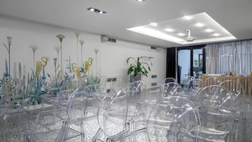 Un salón de conferencias con sillas de plástico transparente, un techo con iluminación empotrada y una pared con un mural floral.
