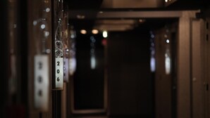 A corridor with numbered doors, likely indicating hotel rooms, leading to a darkened area beyond. - Le Rex Hotel (Tarbes)