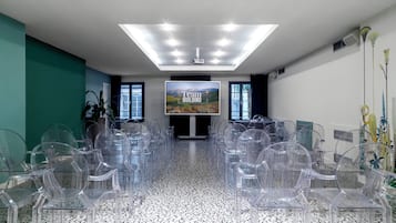 A conference room with a large screen displaying 'Team Building', clear plastic chairs arranged in rows, a ceiling with recessed lighting, and a patterned floor.