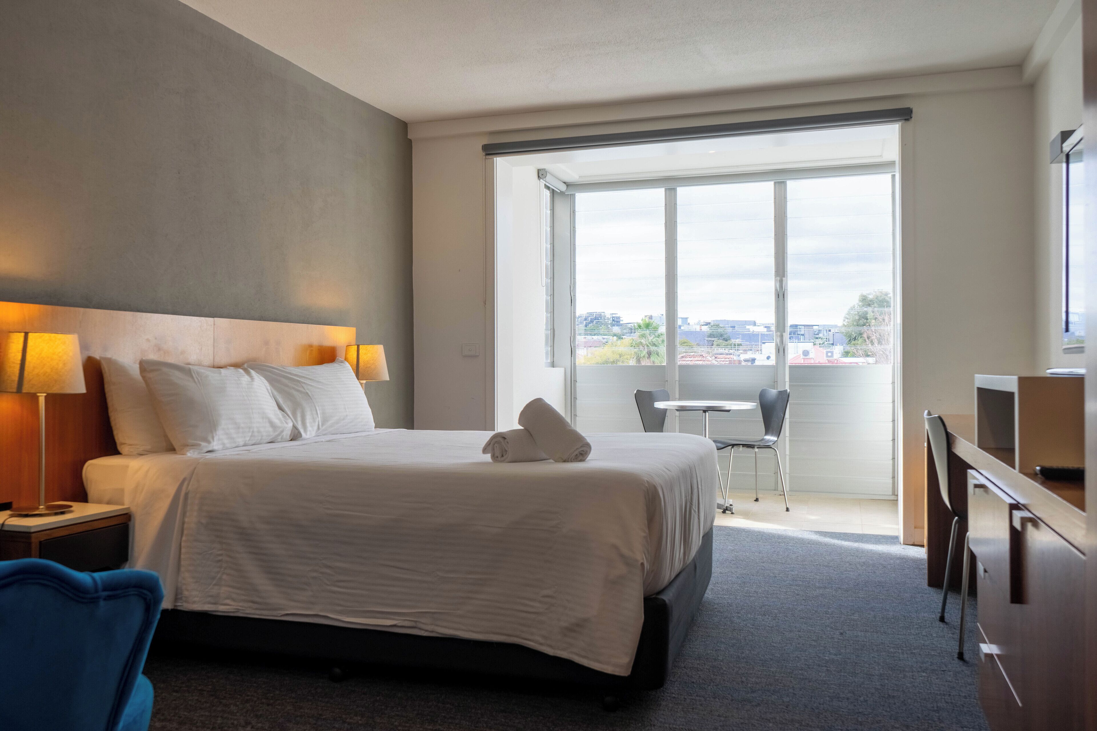 Une chambre d’hôtel avec un grand lit, un bureau, une chaise, une petite table et une fenêtre donnant sur la ville.