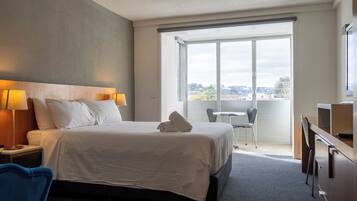 Une chambre d’hôtel avec un grand lit, un bureau, une chaise, une petite table et une fenêtre donnant sur la ville.
