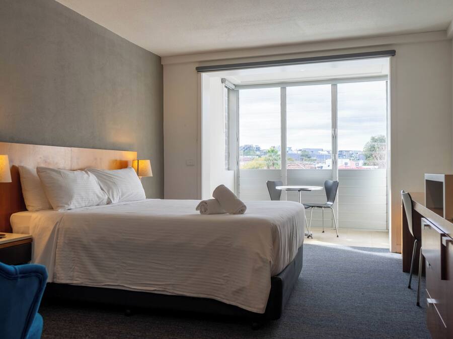 Une chambre d’hôtel avec un grand lit, un bureau, une chaise, une petite table et une fenêtre donnant sur la ville.
