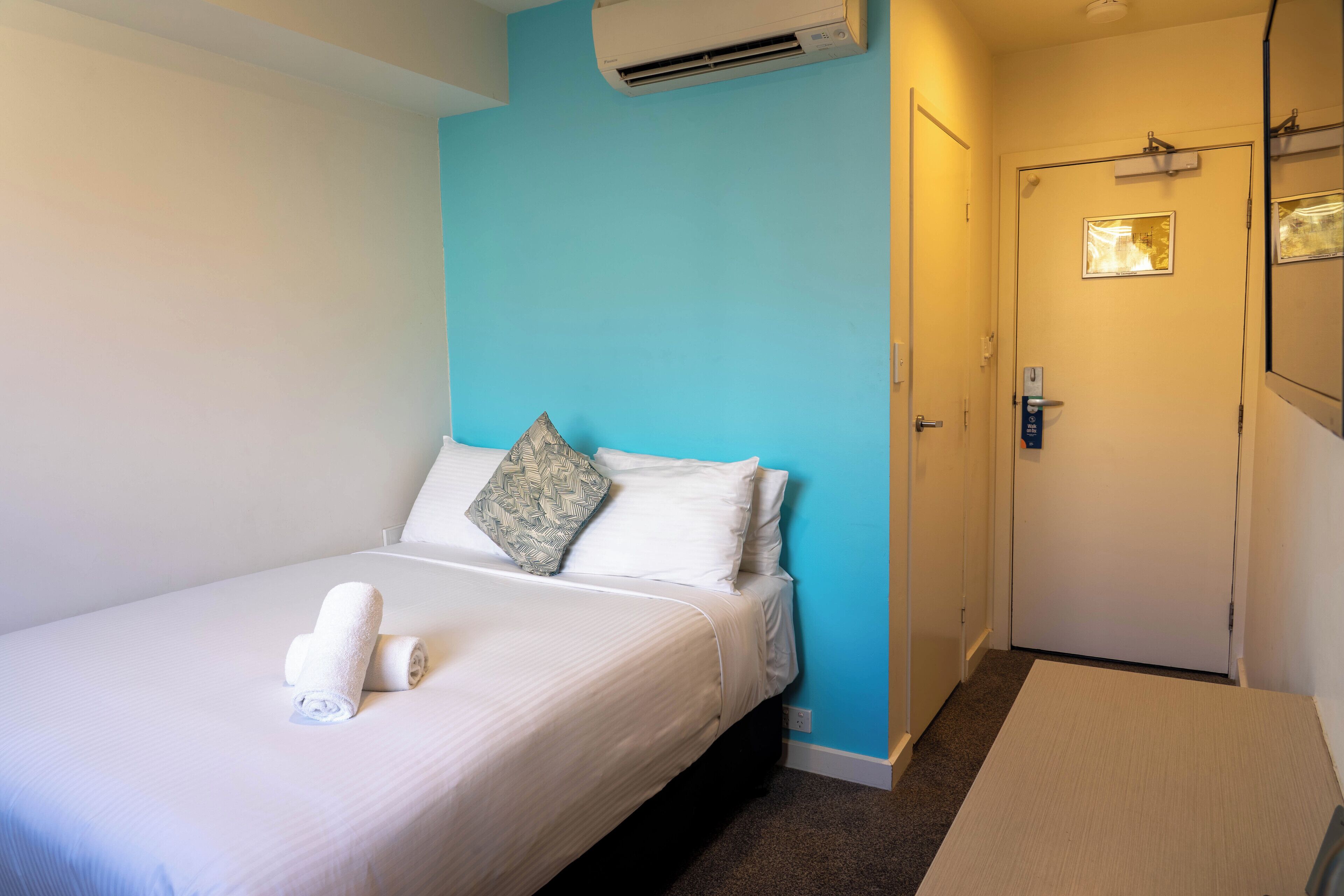 Habitación de hotel con una cama, pared decorativa azul, una puerta y un equipo de aire acondicionado.