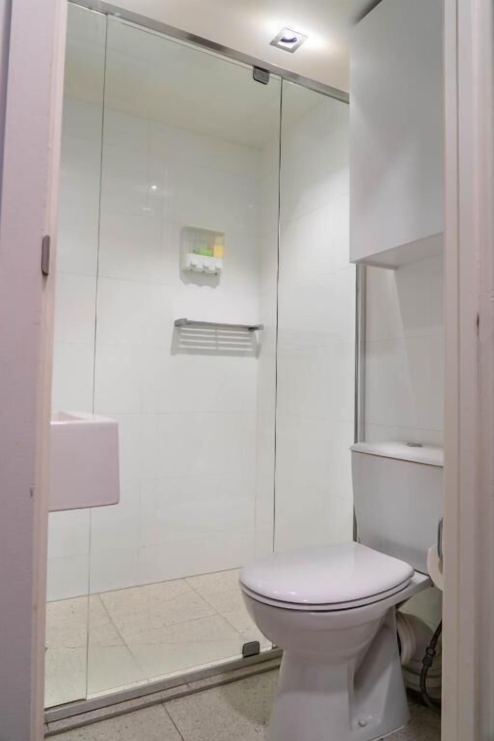 Un baño moderno con ducha de vidrio, inodoro blanco y un lavamanos pequeño.