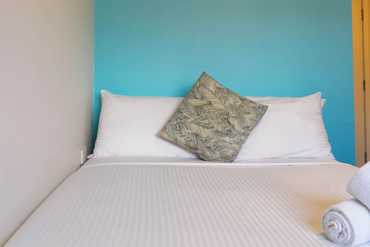 Cama bem arrumada com travesseiro estampado, manta branca e toalha enrolada.